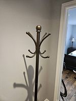 Full view of black metal coat and umbrella stand with multiple curved hooks for hanging items.
