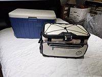 Photo showing two coolers: a large blue and white hard cooler by Coleman in background, and a beige and black soft cooler by Titan in front.