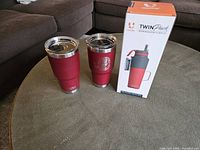 Two red Yeti travel mugs and boxed grey/red insulated bottle displayed on table.