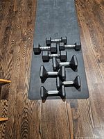 Six hex dumbbells in pairs of 12, 15, 20, 25 lb on a black Peloton mat over wood floor
