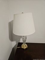 Full view of the Waterford crystal lamp with white shade on a dark wood surface against a plain wall.