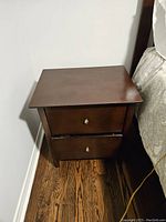 Front view of the dark brown night table showing two drawers and metallic knobs.