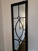 Full view of the tall rectangular metal framed mirror on a wall showing decorative geometric metal pattern dividing the reflective surface.