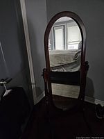 Photo showing the full-length arched dressing mirror in wood frame in a bedroom setting with swivel supports making the mirror adjustable.