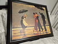 Framed print showing two couples dancing with black umbrellas on a beach, sunlight casting shadows and reflections on wet sand