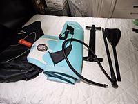 Rolled light blue and white inflatable paddle board, detached black fin, black pump, and black dual-piece paddle laid out on a white surface.