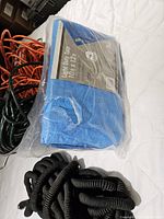 Blue polyethylene tarp 10x12 ft in original packaging with coiled black and orange extension cords also visible