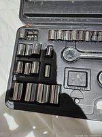 Close-up photo of the ratchet socket set inside the open black plastic carrying case, showing multiple chrome sockets and ratchet handle, some sockets appear missing.