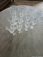Ten crystal champagne flutes arranged on a textured table, showing clear crystal with cut pattern details.