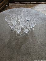 Eight clear crystal iced tea glasses arranged in a cluster on a textured grey surface, showing detailed cut glass patterning and starburst bases.