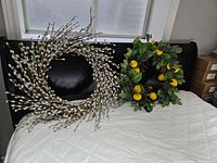 Two door wreaths displayed on a bed; spring wreath made of pussy willow branches and summer wreath with greenery and yellow lemons visible