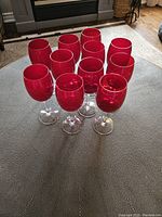 Set of 11 ruby red colored wine glasses arranged on a table showing the clear stems and bases with deep colored bowls.