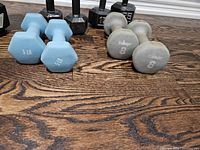 Photo showing light blue 5 lb neoprene dumbbells and gray 8 lb Bollinger neoprene dumbbells on wood floor.