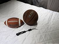 Nike Elite Composition basketball next to Mikasa football and black air pump on white quilted surface.