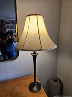 Full view of the table lamp showing its beige linen shade and tall black hammered metal base on a wooden surface.