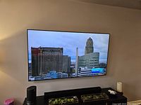 Front view of the mounted 76 inch Samsung television with power on, displaying a city skyline.