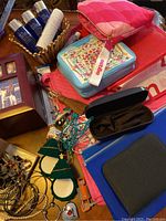 Photo showing assorted bags, small tin box, toiletries, jewelry organizer box, and various jewelry pieces spread on a table.