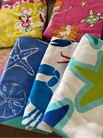 Five assorted beach towels folded, showing colorful marine and cartoon designs