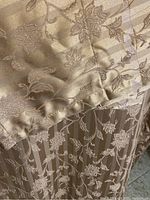 Close up of beige gold fabric showing floral embroidery and striped pattern on drapes.