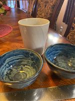 Two handmade ceramic bowls with blue glaze inside and one white flower pot on wood surface with ruler in view.