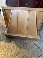Photo of the oak hood showing the slanted panel design and wood grain, positioned on a tiled floor.
