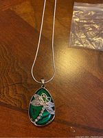 Front view of the dragonfly pendant on a green natural stone teardrop attached to the silver-tone chain.
