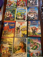 Twelve children's DVDs arranged on a surface showing covers of popular animated movies including Scooby-Doo 2, Shrek series, The Penguins of Madagascar, Stuart Little editions, Despicable Me, The Tale of Despereaux, Frit, and Once Upon a Forest.