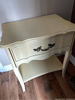 French Provincial cream-colored night stand showing the drawer and curved design with minor surface scratches.