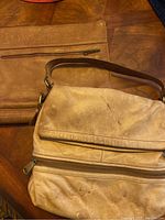 Medium brown leather file holder with front zipper pocket, on wood surface, showing wear and signs of use