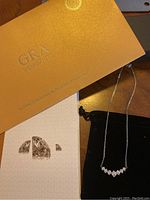 GRA Moissanite branded box with product information and a black velvet pouch holding the necklace with seven moissanite stones on chain.