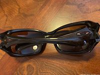 Oakley sunglasses showing dark brown glitter wraparound frames with visible logo on the arms and scratches on the frame.