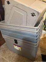 Stacked view of multiple gray plastic storage totes showing lids and sides with integrated handles and locks.