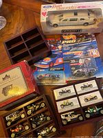 Lot showing boxed white Kinsmart Beat Limousine toy car, Hot Wheels Pro Racing NASCAR cars, vintage model cars sets in collector boxes, and wooden storage box.