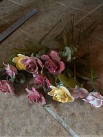 Photo showing group of porcelain roses with stems and leaves on tiled floor, some leaves detached.