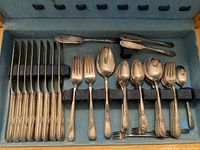 Full overview of most silverware pieces arranged in wooden chest with blue velvet lining showing knives, forks, spoons, and spreaders