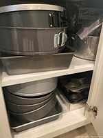 Shelf with stacked metal springform pans, square pan, and other baking pans