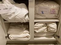 Photo showing white twin mattress pad and down winter comforter packaged and labeled inside a cabinet.