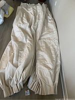 Full view of two cream-colored blackout curtain panels laid out flat on the floor showing their length and fabric texture.