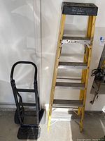 Photo showing Werner fiberglass ladder standing next to black Harper hand truck with two wheels