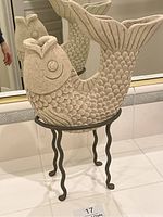 Front and side views of koi fish sculpture showing stone texture, scale details, and black metal wavy leg stand.