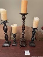 Photo of four large dark wooden candle holders with beige pillar candles, showing both close-up and overall view on table
