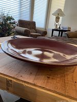 Side angle of the large rust colored glazed stoneware bowl showing smooth glossy finish and curved edges.