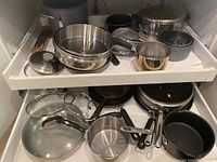 Full view of pots and pans including stainless steel and non-stick cookware, glass lids, strainers and steamers, displayed in a white drawer.