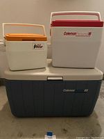 Three Coleman coolers stacked: large Polylite 68 cooler at bottom, medium Personal 16 cooler and small Lil Oscar cooler on top