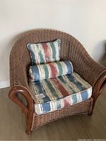 Front view of wicker chair showing cushions and pillows with striped fabric pattern in blue, green, cream, and reddish tones.