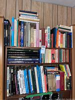 Three wooden shelves filled with assorted hardcover and paperback books, plus a stack on top. Visible spines include train histories, atlases and various volumes.