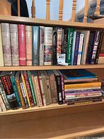 Book shelf with assorted hardcover and softcover books covering fiction and non-fiction including classics and quilting related titles.