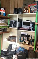Photo showing shelves with various electronics including speakers, portable DVD player, radios, clocks, and small accessories.