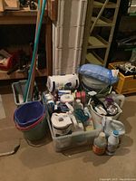 Wide view of entire cleaning supplies lot including buckets, paper products, and metal utility shelf visible in background.