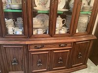 Wood cabinet filled with the dinnerware set pieces including plates, mugs, bowls, teapot, and serving items.